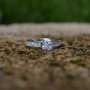 Cushion cut diamond engagement ring with round diamonds in shared prongs in shank with milgrain beading