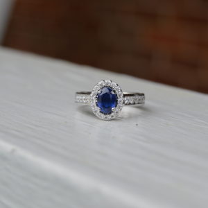 Custom designed oval sapphire and diamond ring in 14kt white gold with diamond halo and channel set diamond shank
